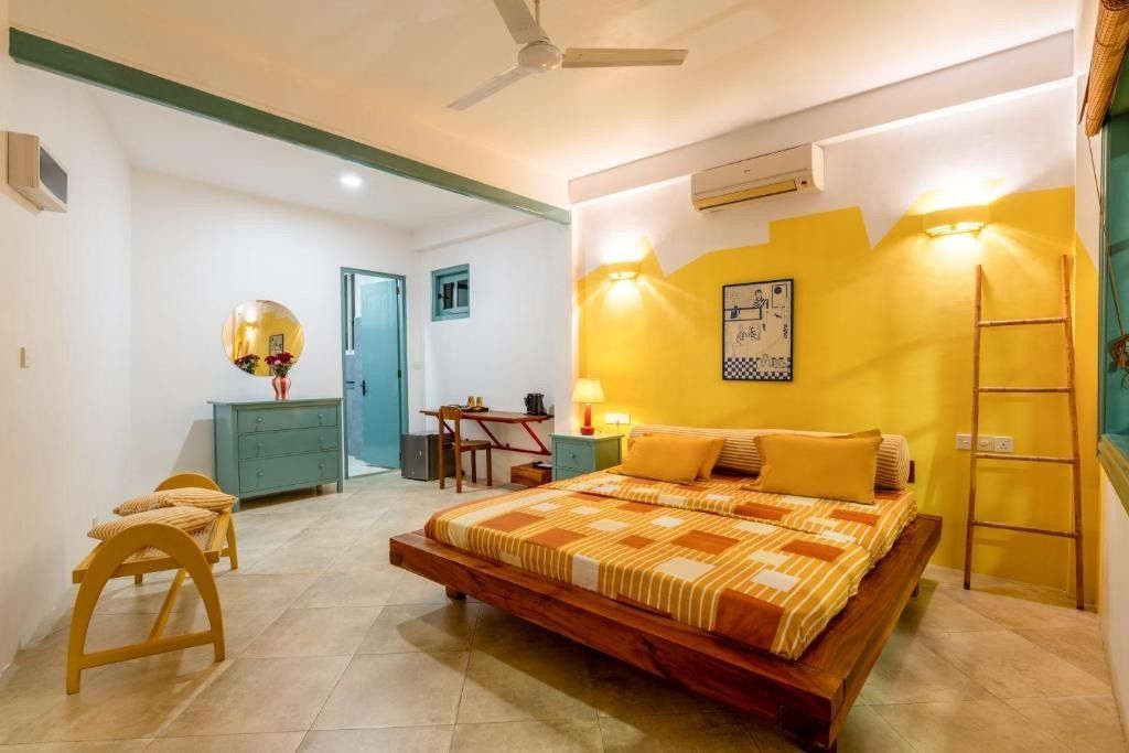 Bedroom with yellow accent wall, wooden bed frame, turquoise furniture, and natural light.