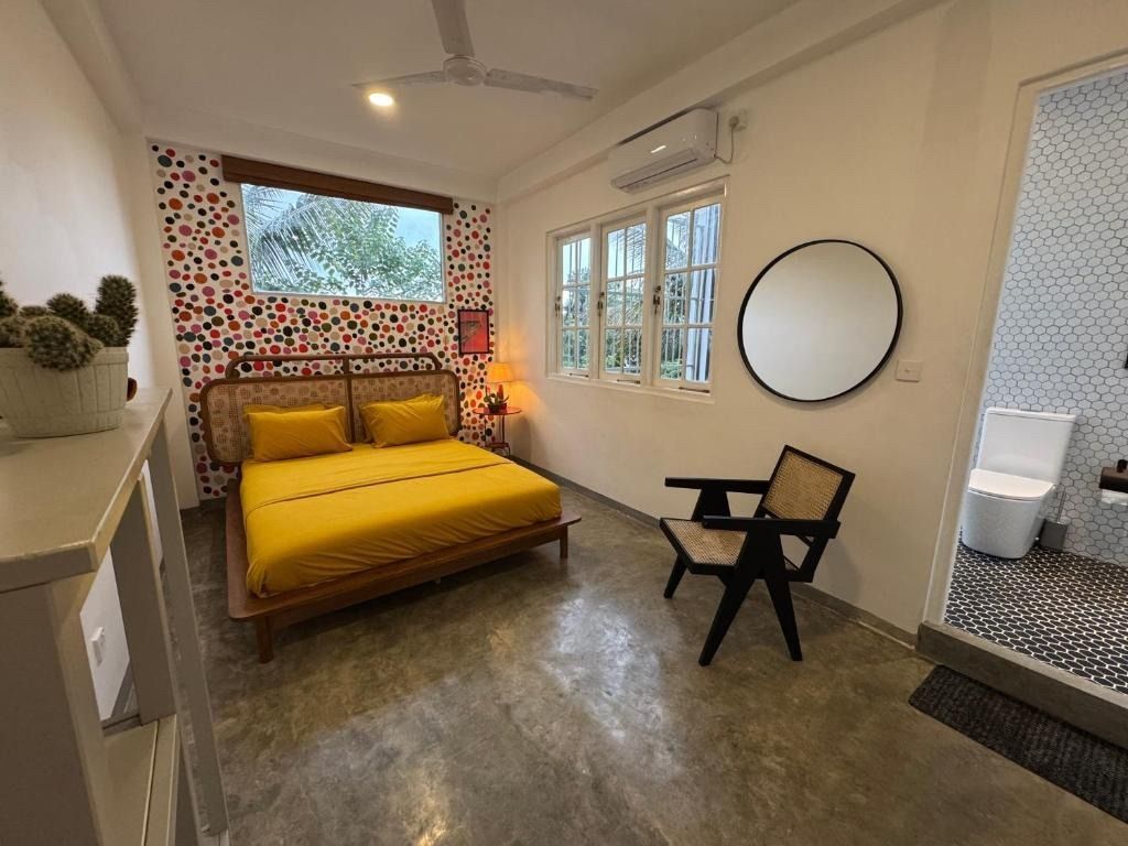 Bedroom with yellow bed, patterned accent wall, round mirror, and a chair.