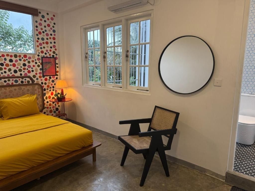 Bedroom with yellow bed, patterned wallpaper, round mirror, and black chair.