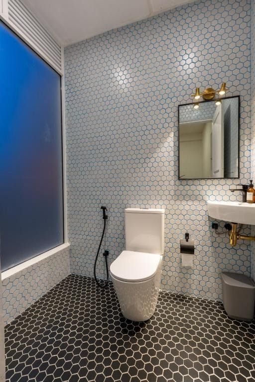 Modern bathroom with blue-tiled walls, black hexagonal floor tiles, a toilet, a mirror, and a frosted window.