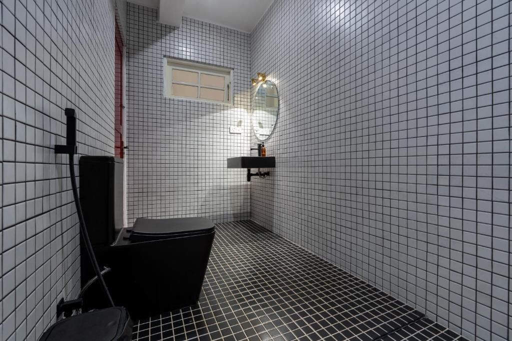 Black and white tiled bathroom with a black toilet, sink, and shower. Mirror reflects light.