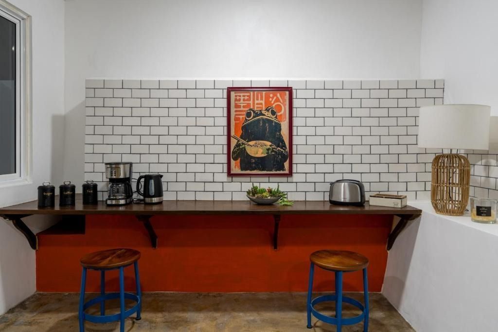 Kitchen counter with appliances and artwork against a brick wall, orange base, and blue stools.