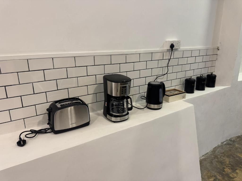 Kitchen counter with appliances: toaster, coffee maker, kettle, and spice jars, against a white brick-style tiled wall.