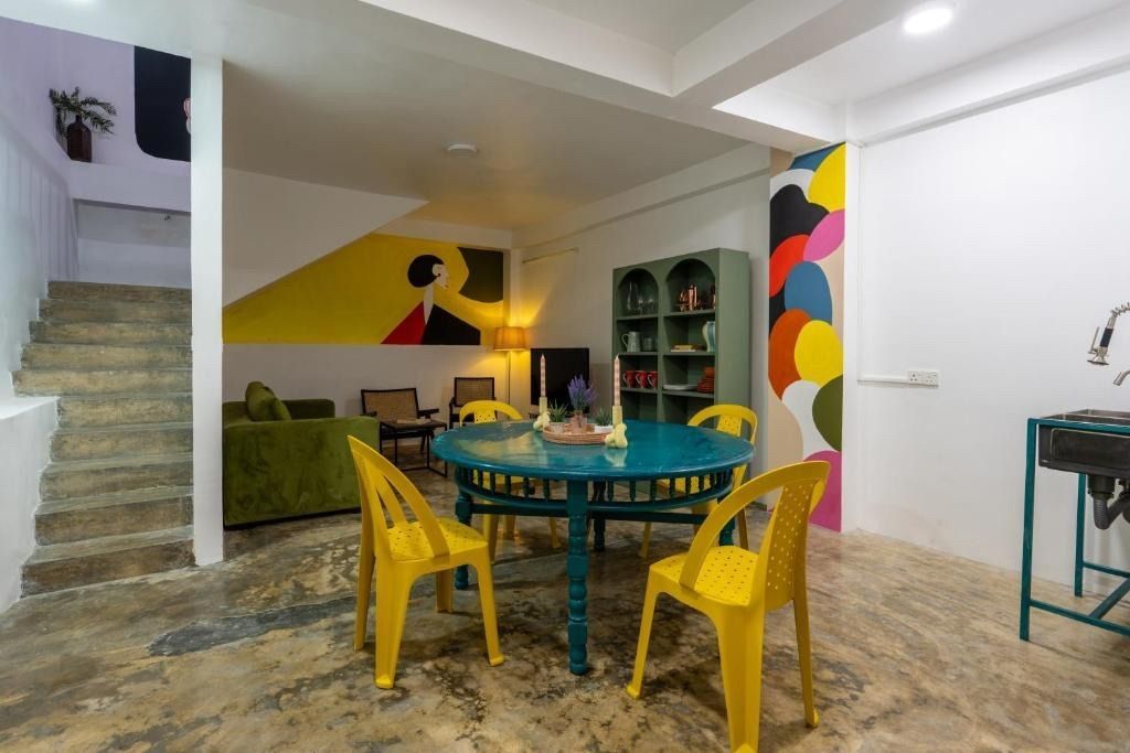 Interior with stairs, blue table, yellow chairs, green couch, colorful wall art, and a storage cabinet.