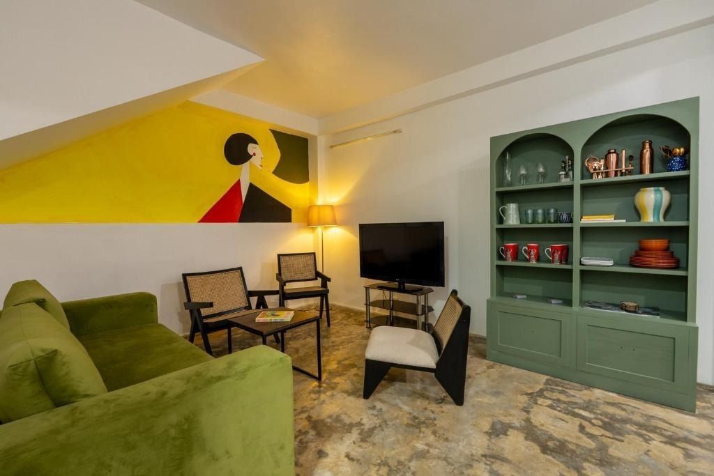 Living room with green sofa, black chairs, artwork, green bookcase, and television.