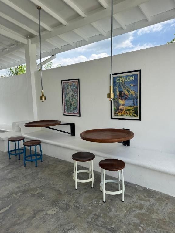 Cafe seating area with white wall, round wooden tables, stools, and Ceylon poster.