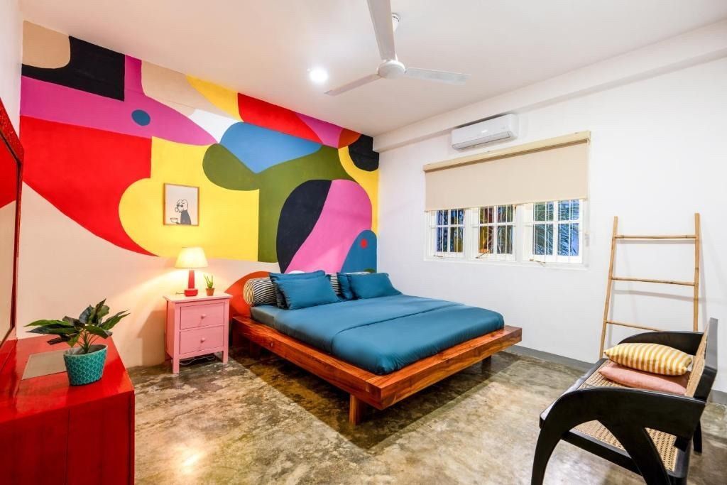 Bedroom with colorful mural, bed, red dresser, pink nightstand, and window.