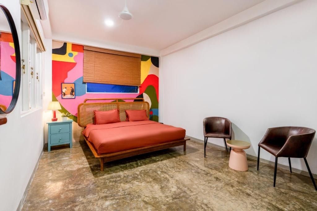 Bedroom with colorful mural wall, bed, chairs, and side table.