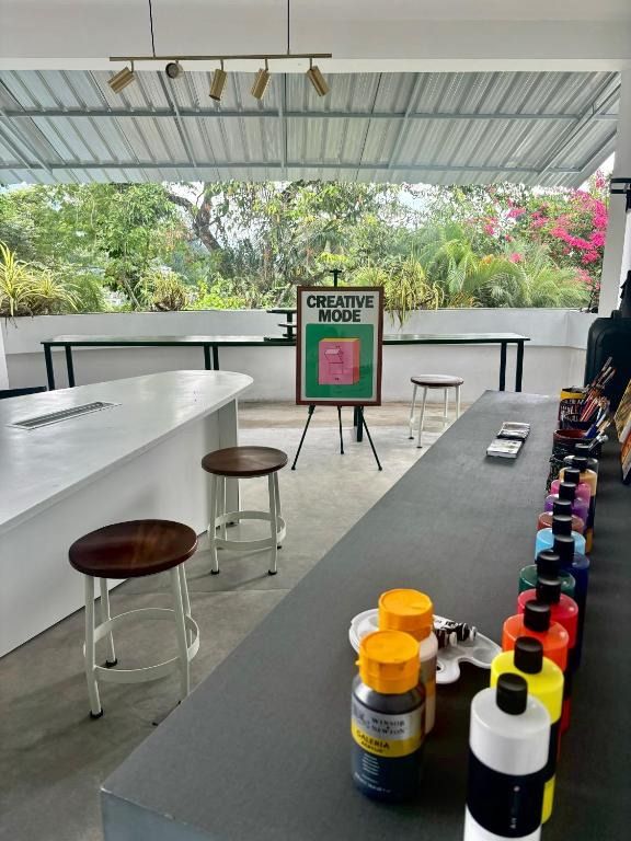 A bright, open art studio with a row of colorful paint bottles, stools, and a framed