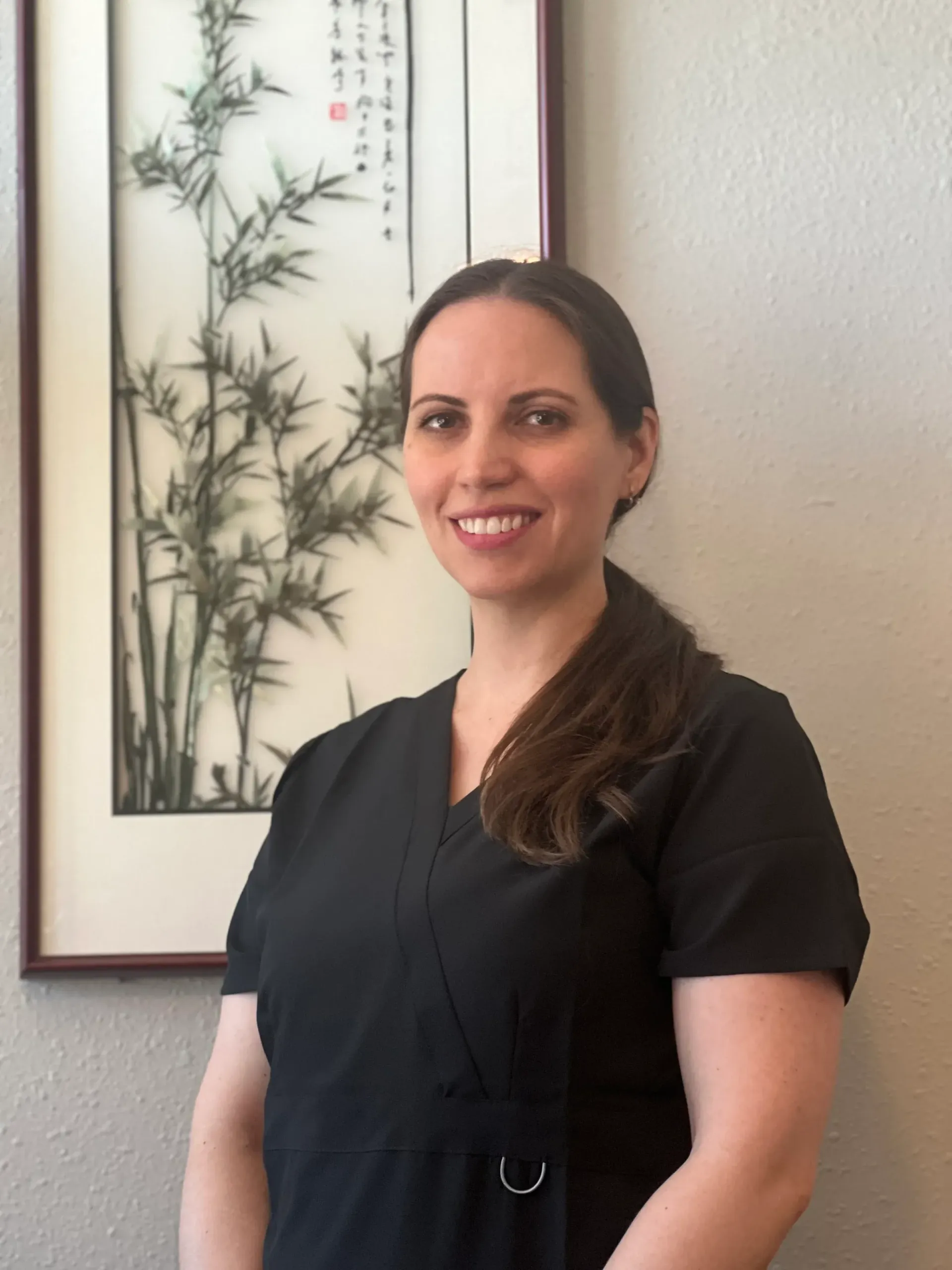 Woman in black uniform smiles in front of a framed bamboo art piece.