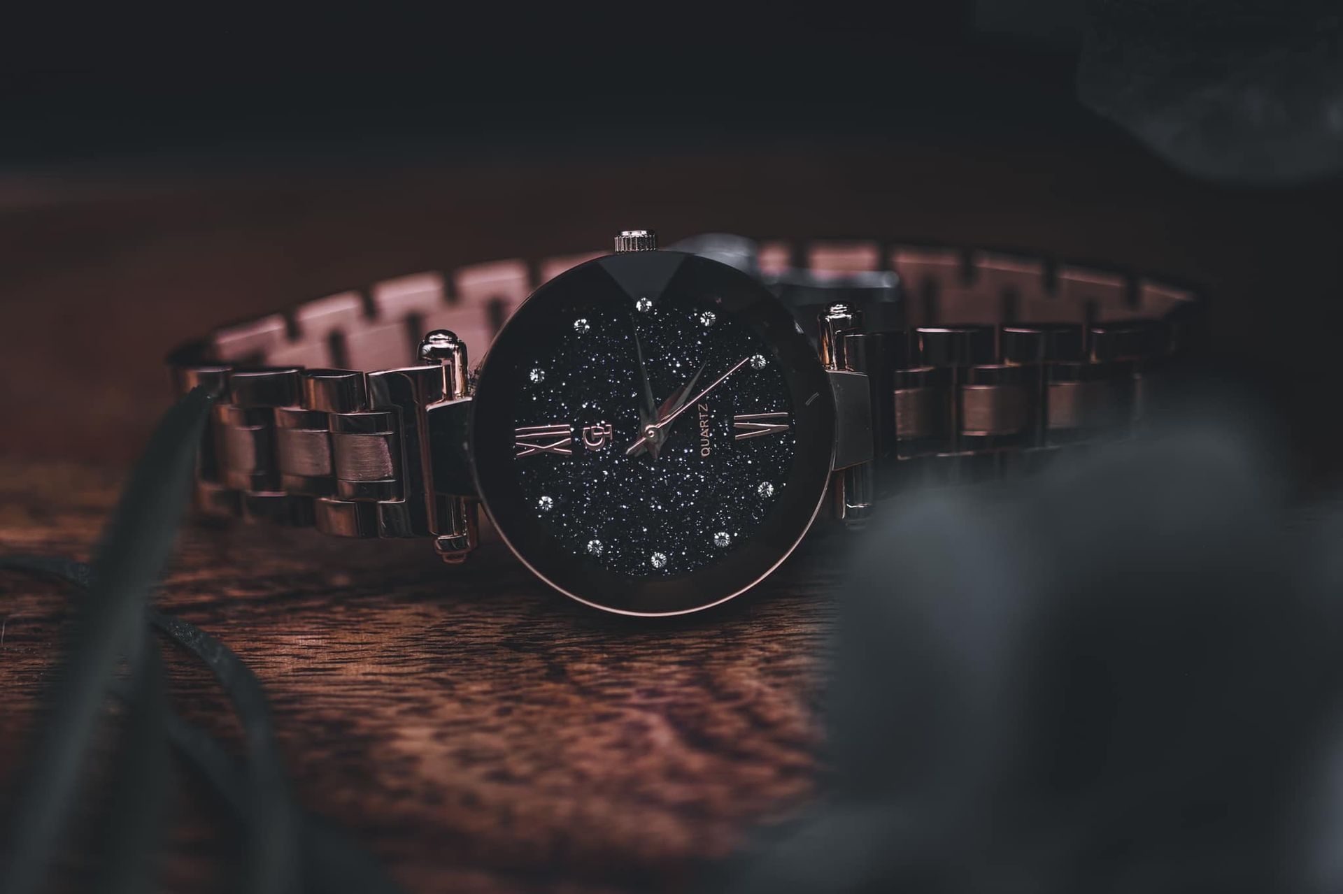 Rose gold wristwatch with dark face and diamond accents on a wooden surface.