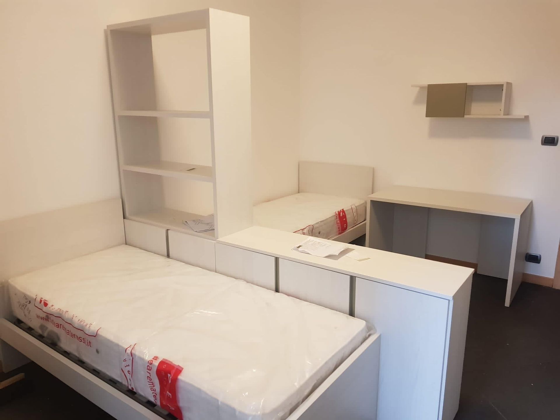 Camera da letto con due letti bianchi, una scrivania e una libreria.