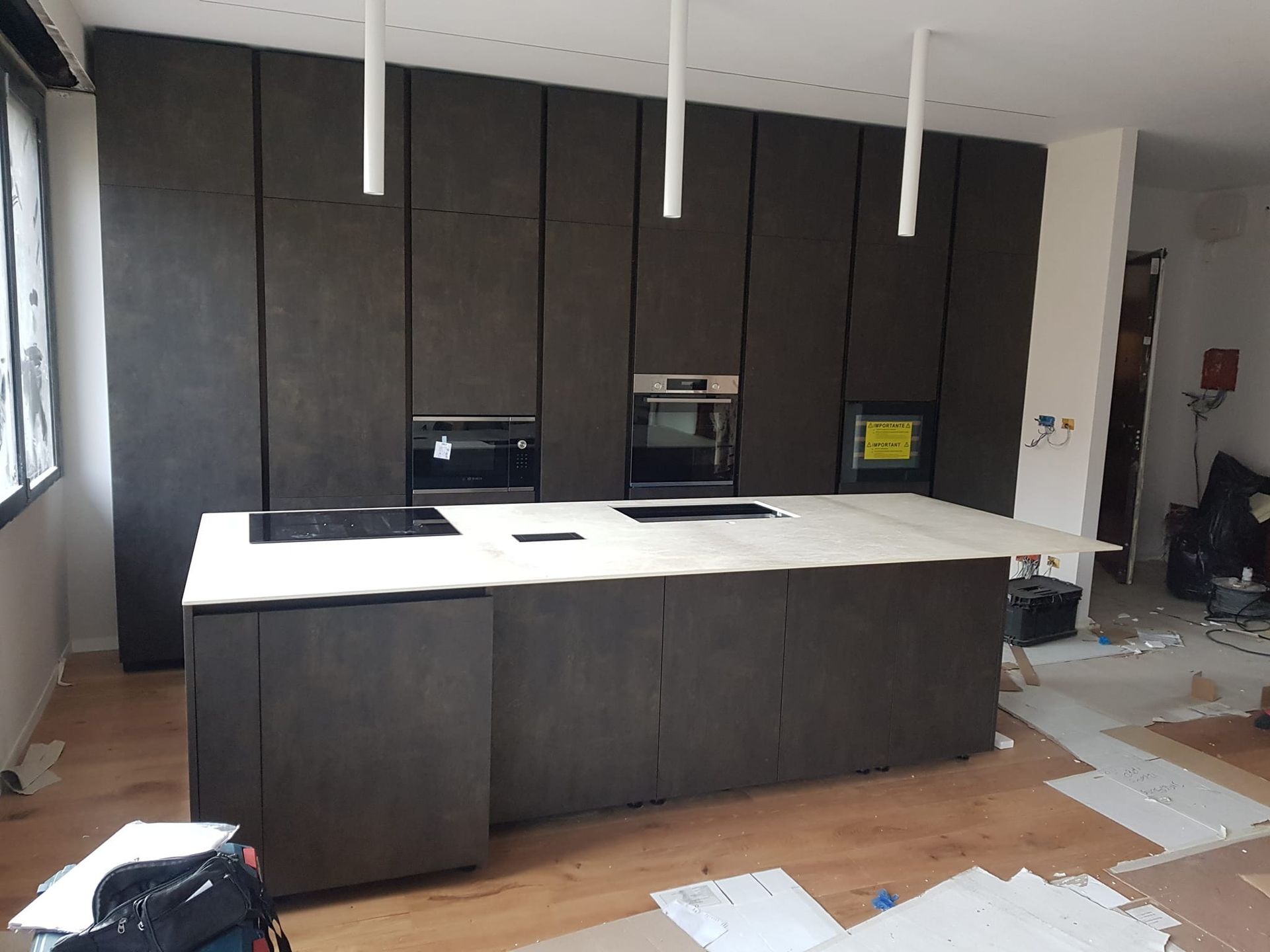 Cucina moderna con mobili scuri, isola bianca con piano cottura e forni incorporati.