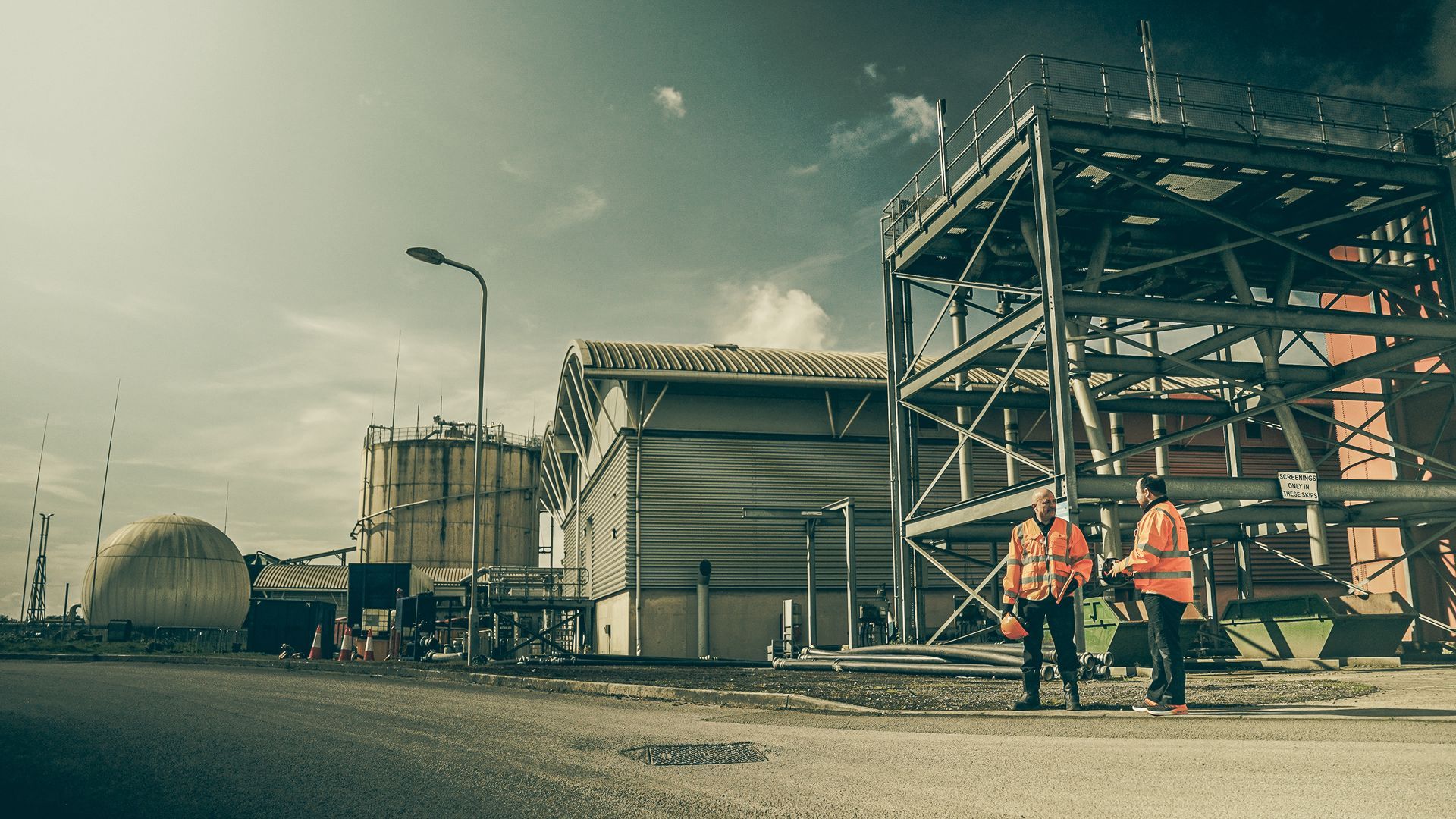 Two safety workers are walking down the street in front of waster water treatment plant.