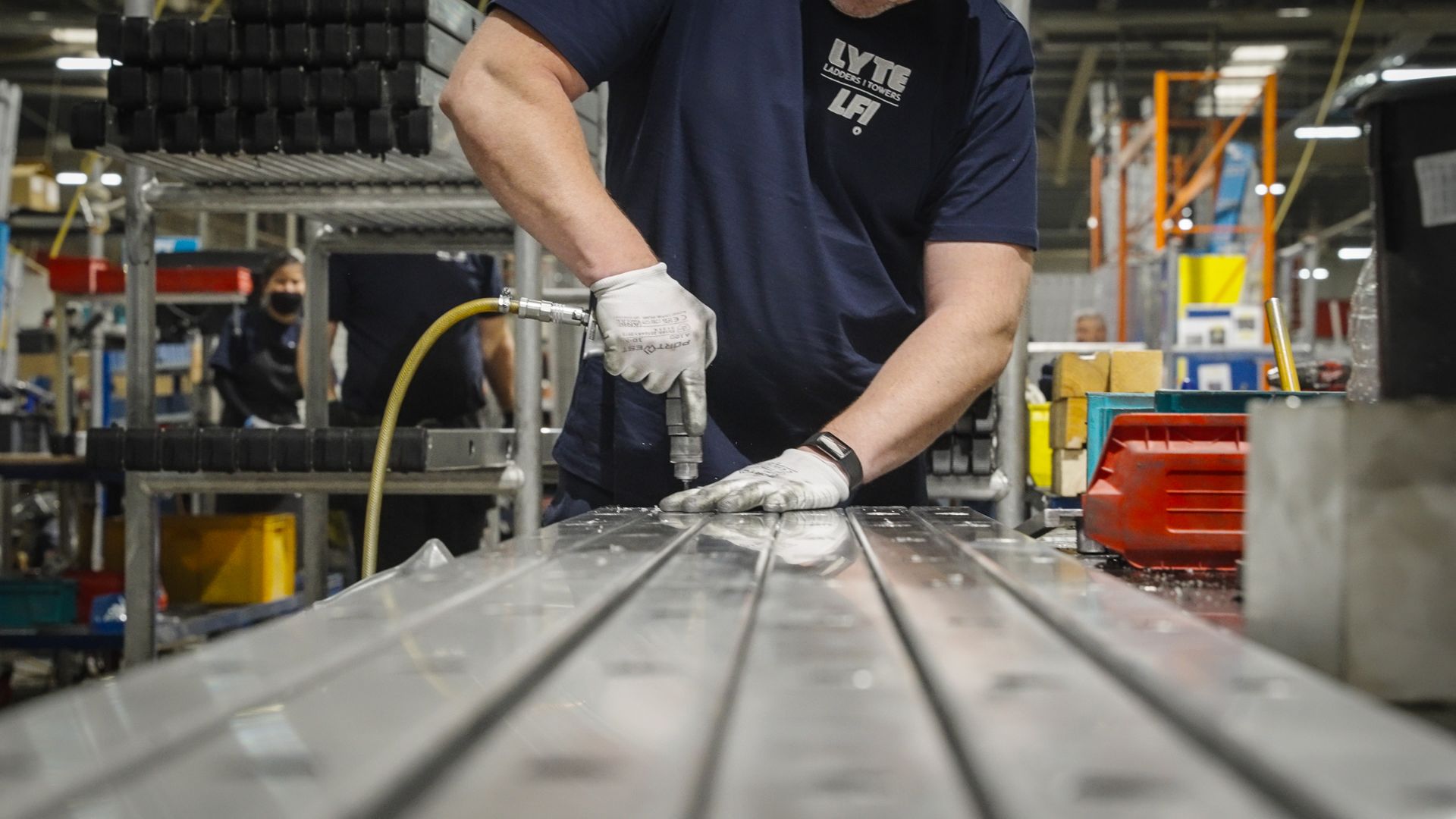 Factory worker using a drill on a metal surface; indoors, focused work.