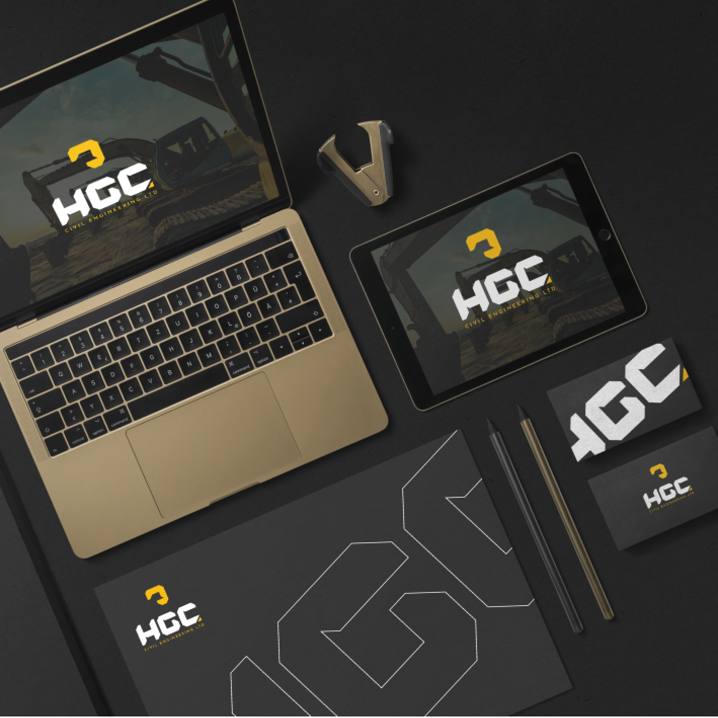 Branded office supplies with HGC logo: laptop, tablet, mouse, notepad, business card, pencil, on black.