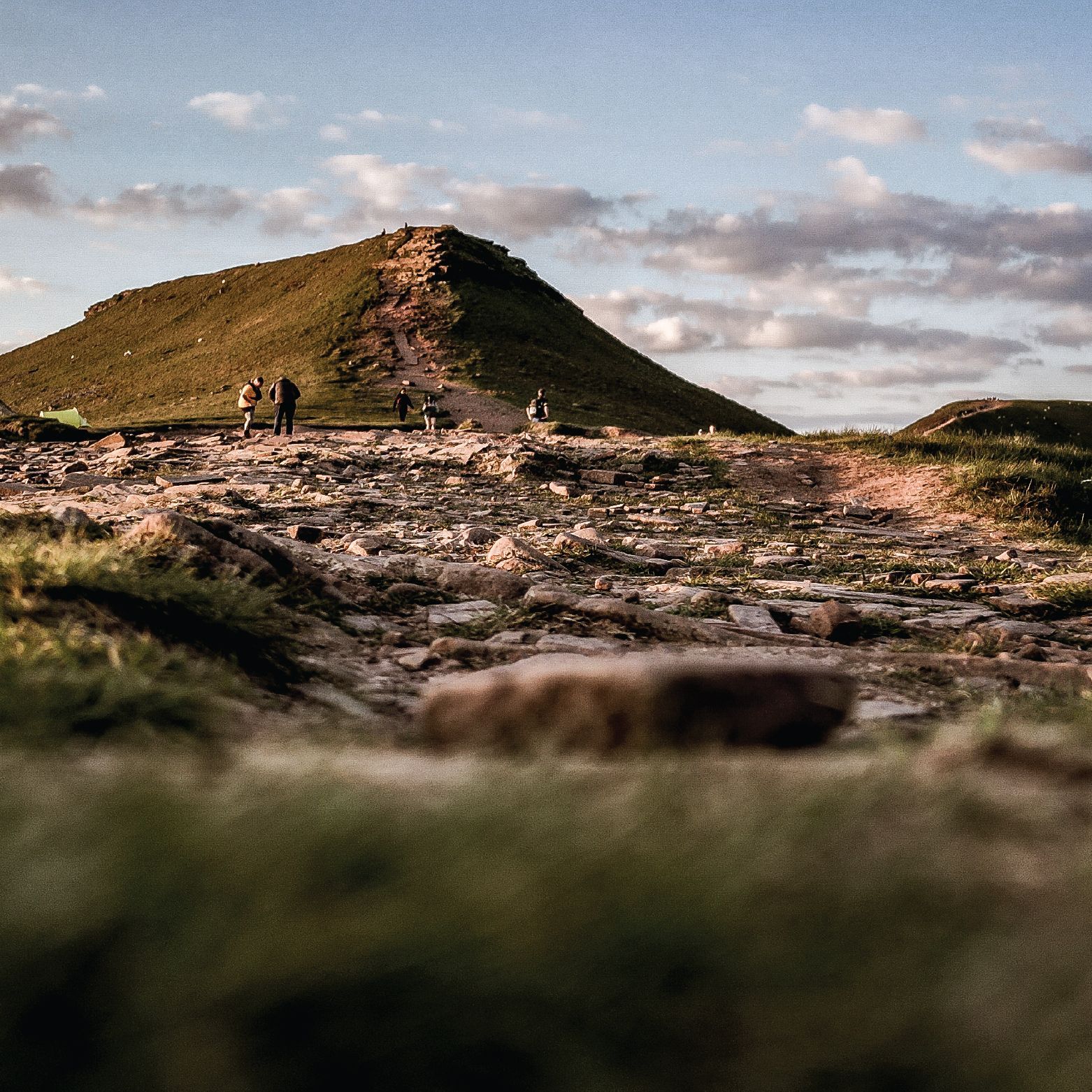 People hiking on a mountain peak under a partly cloudy sky.