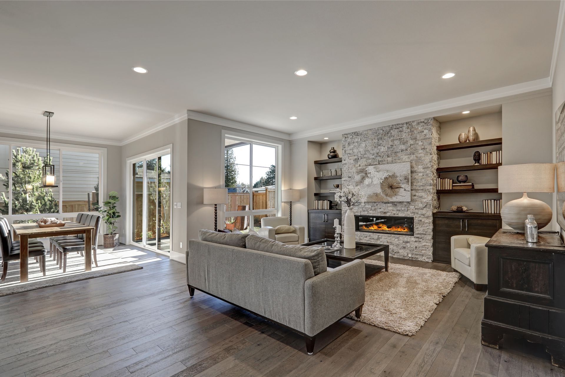 Spacious living room with gray sofa, fireplace, and dining area with hardwood floors and outdoor access.