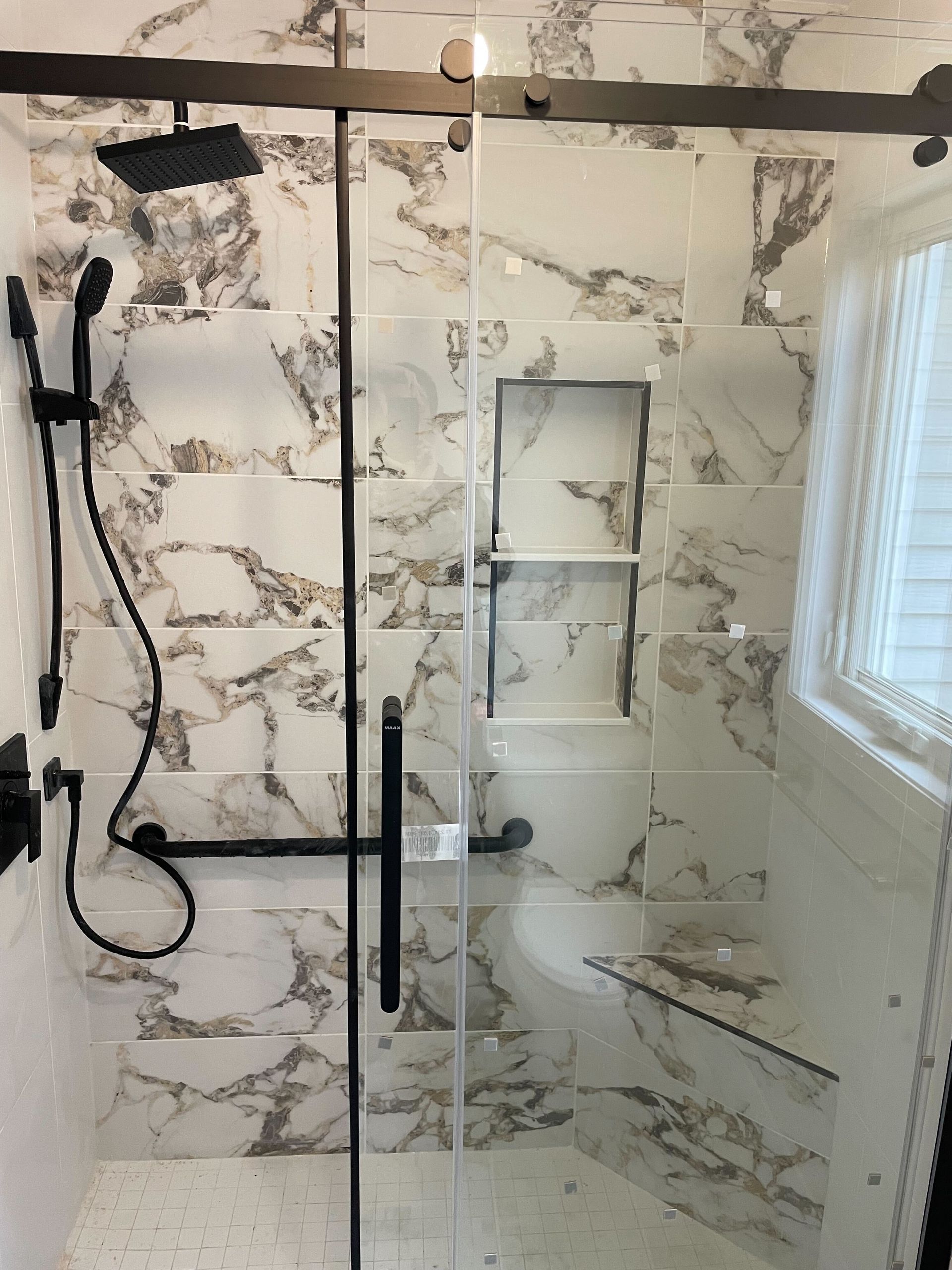 Shower with marble-look tile, dark metal fixtures, and glass doors; features a built-in shelf.