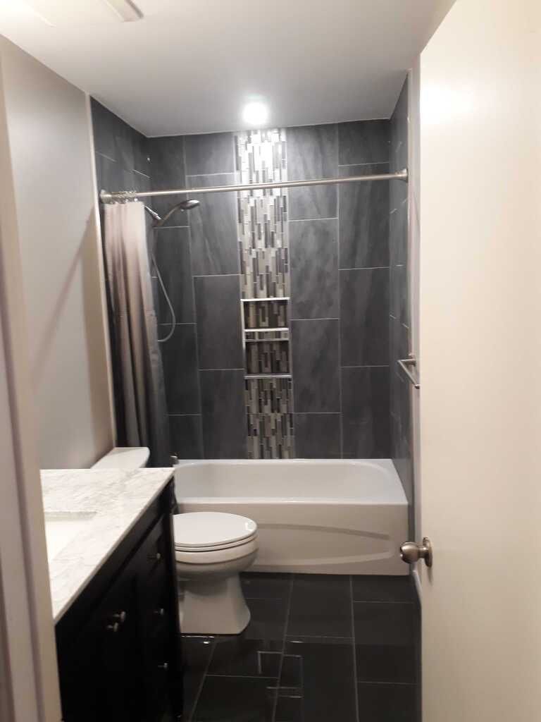 Bathroom with dark tile, a white tub, and a vanity.