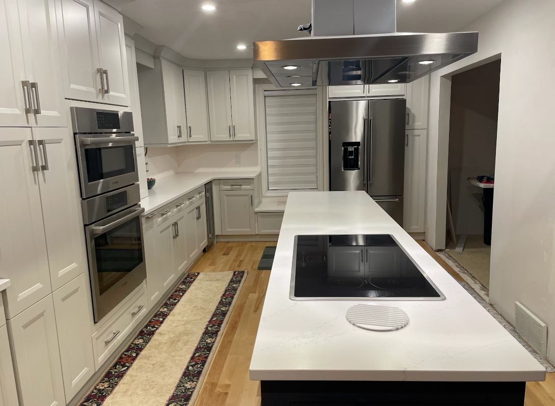 Wooden kitchen countertop with white subway tile backsplash, cooktop, and plant.