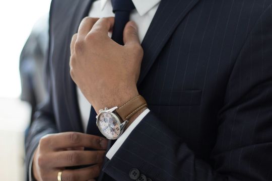 A man in a suit and tie is adjusting his tie while wearing a watch.