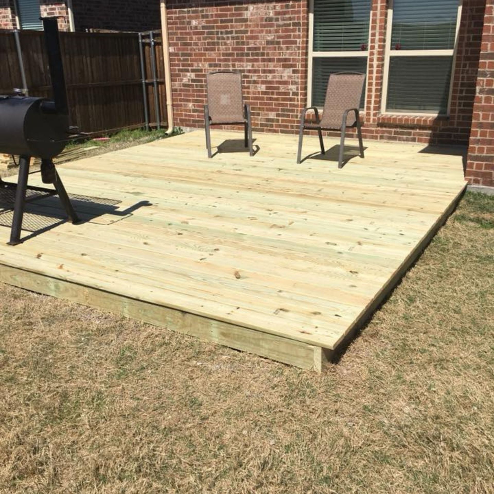 Masters Touch Roofing - A wooden deck with chairs and a grill in front of a brick house.