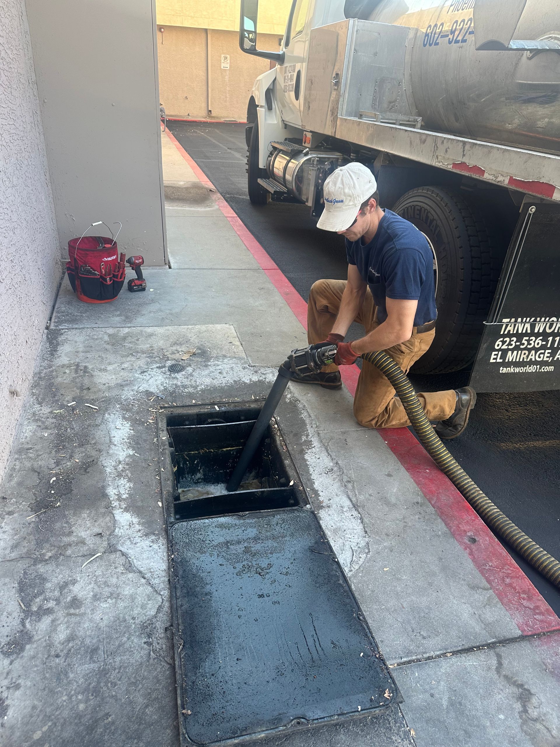 A man is kneeling down next to a truck and pumping water into a manhole cover.