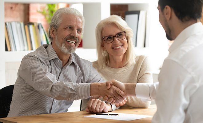 Older couple smiling, shaking hands with a person, indoors.