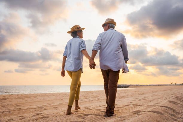 Couple holding hands walking on a beach at sunset.