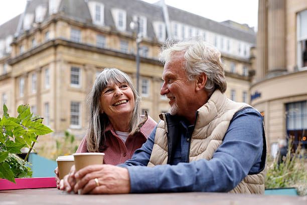 Two people smile at each other, holding coffee cups at an outdoor cafe.