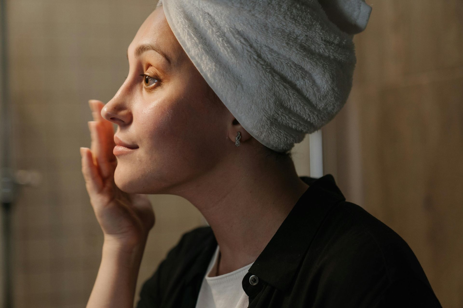 Une femme avec une serviette enroulée autour de sa tête regarde son visage.