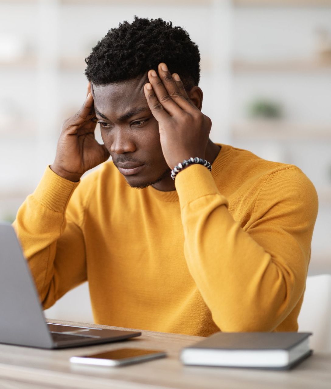 Un homme portant un pull jaune est assis à un bureau et utilise un ordinateur portable.