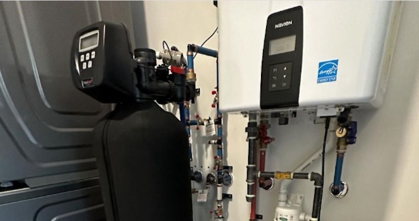 A water softener is sitting next to a water heater in a room.