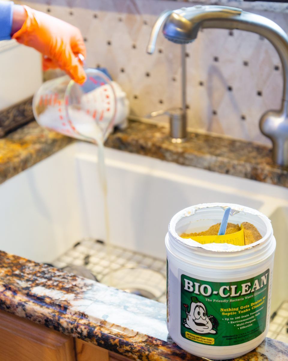 Person pouring cleaning powder into a kitchen sink from a measuring cup, next to the container of 