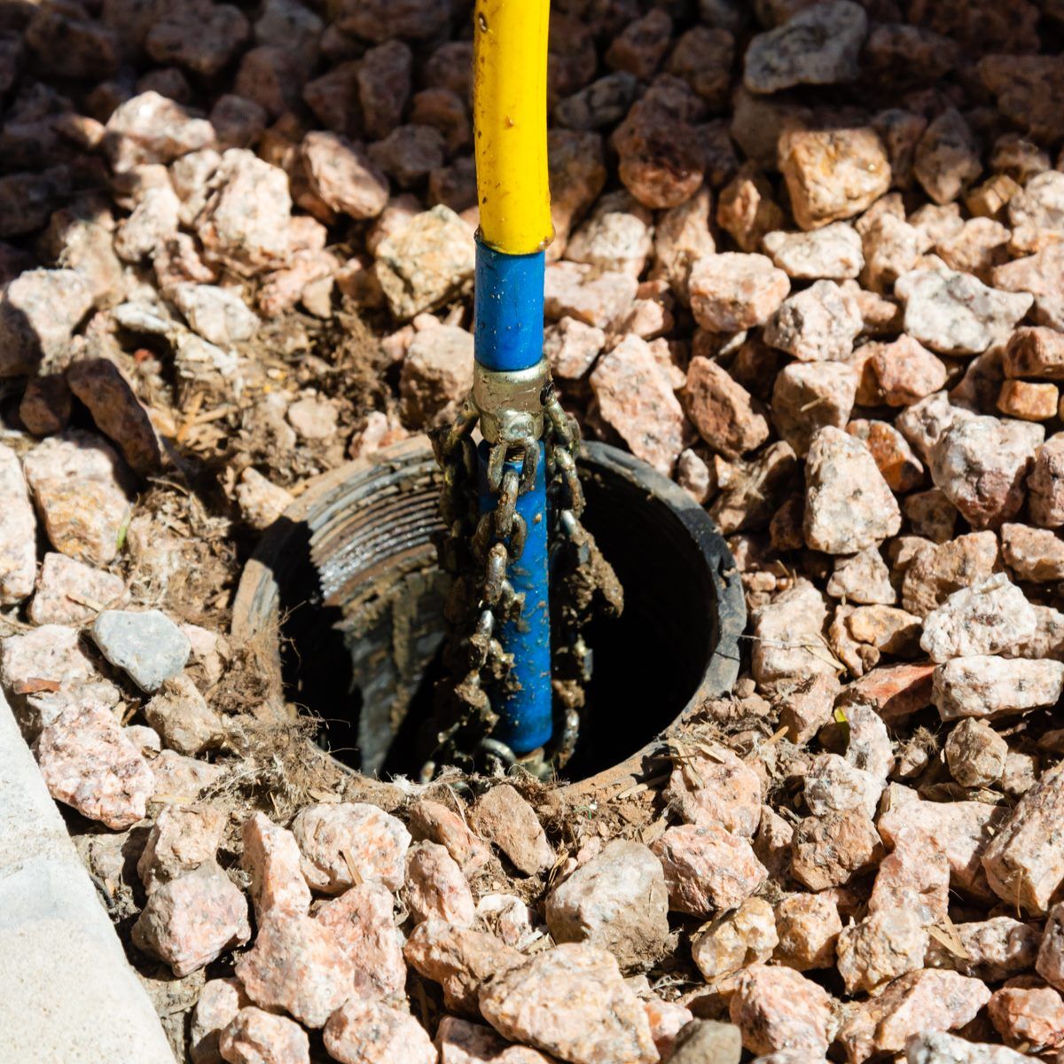 A tool with a chain is inside a dark well. Pebbles surround the well.