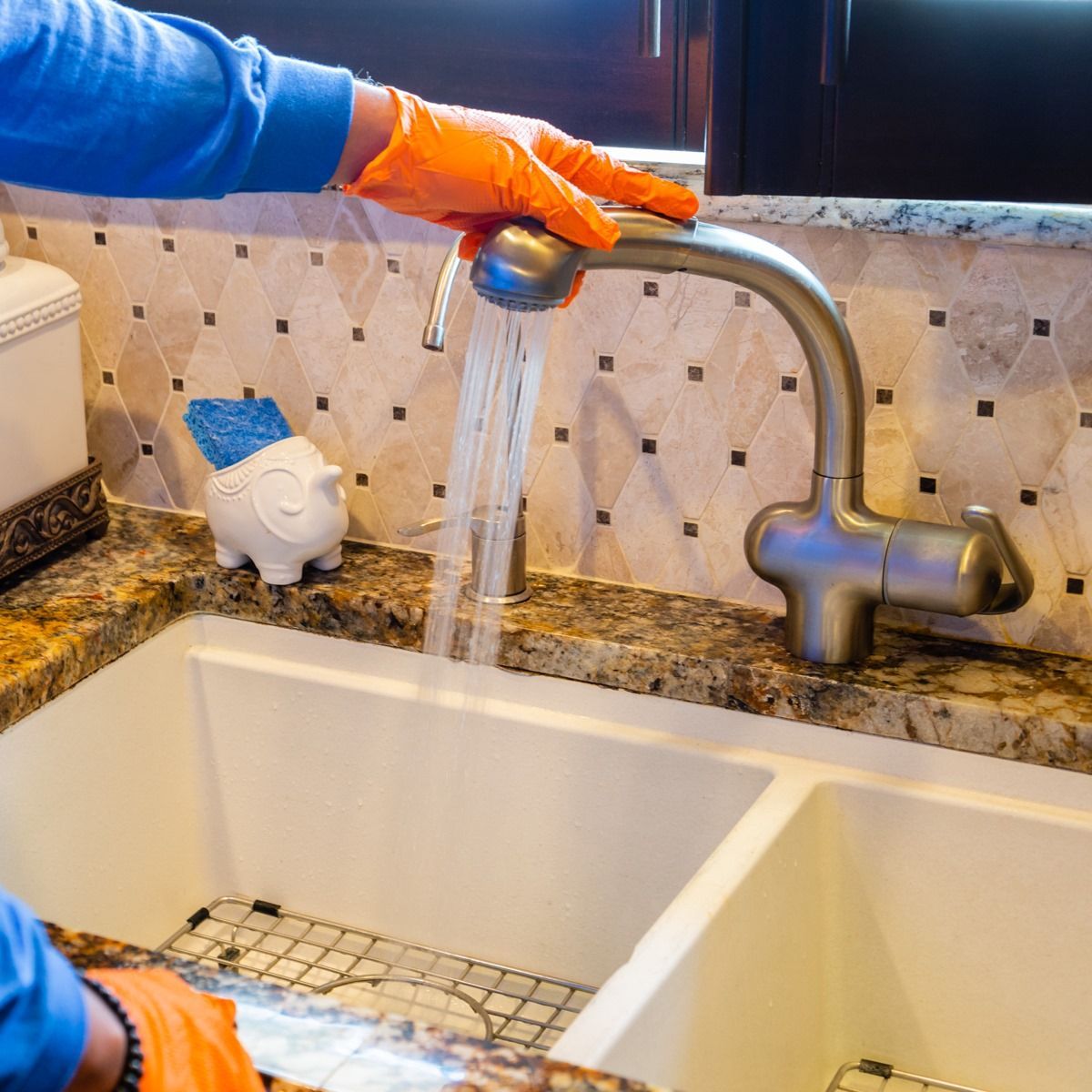 Person wearing orange gloves washing dishes in a double sink with running water.