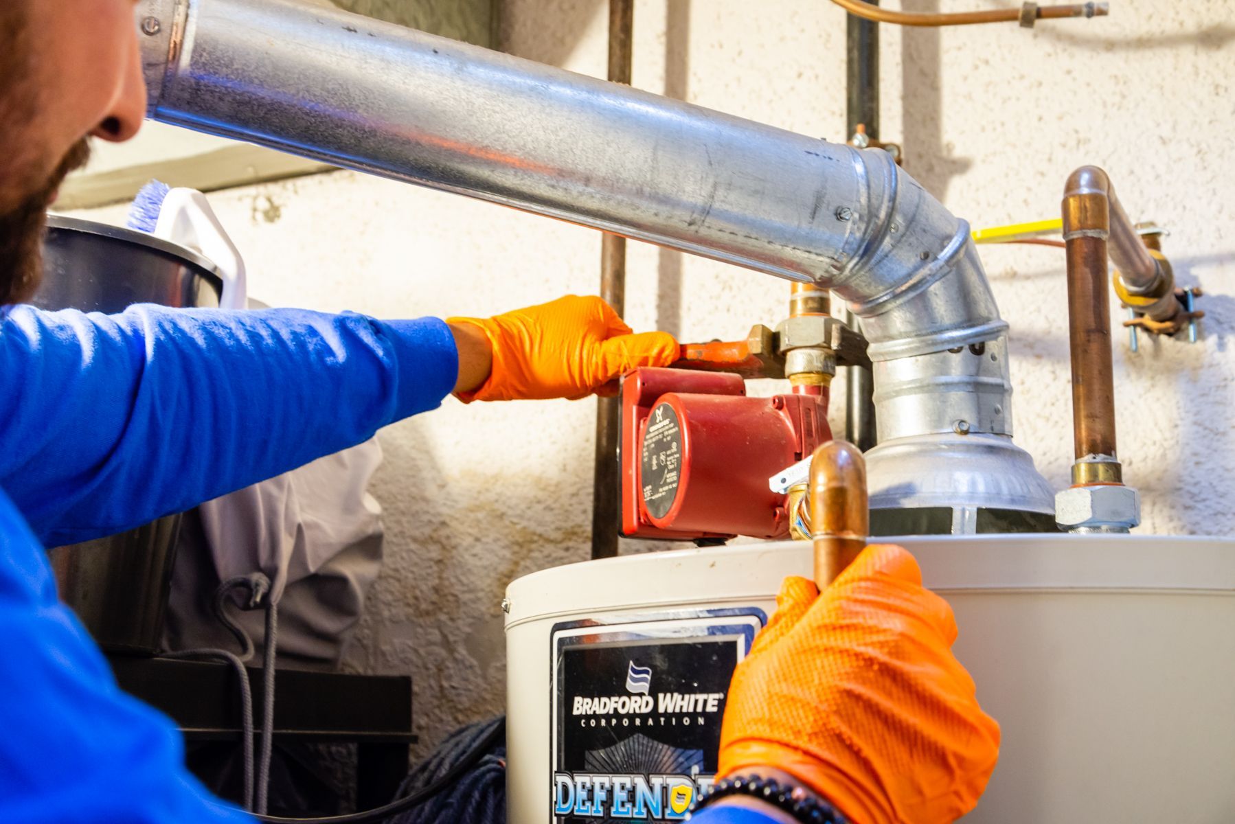 Person using pliers to work on plumbing near a hot water heater.