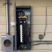 Open electrical panel with exposed wiring mounted on a beige exterior wall.