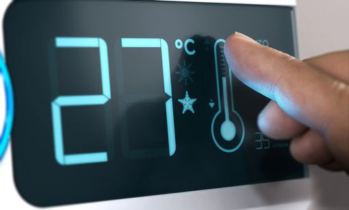 Un dito tocca il display di un termostato digitale impostato a 27 °C
