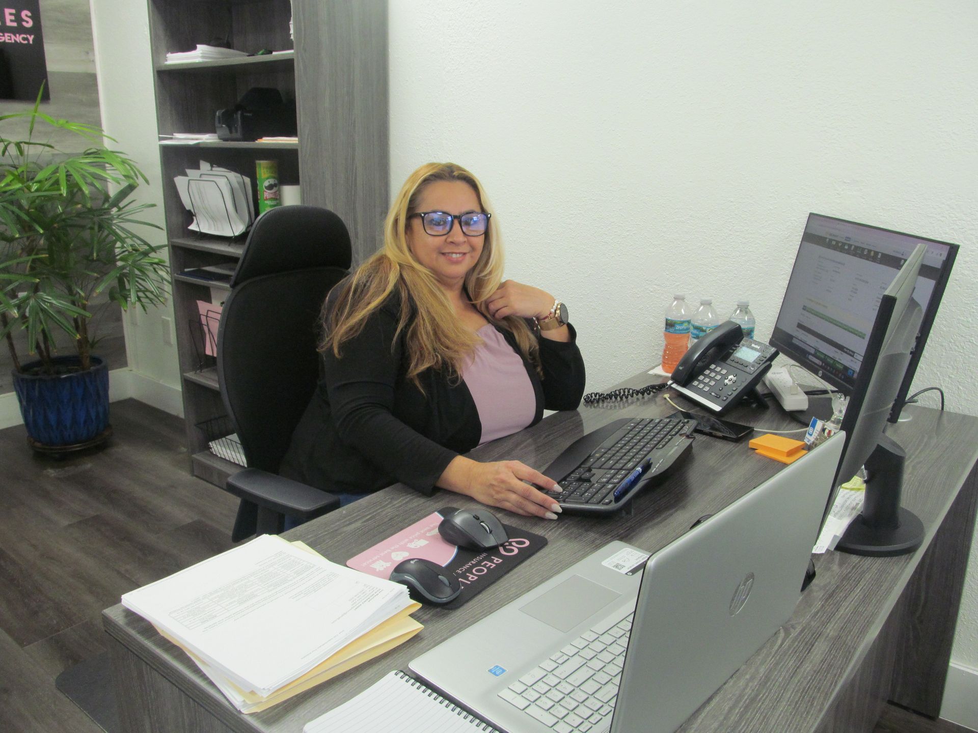 A woman is sitting at a desk with a computer and a laptop.