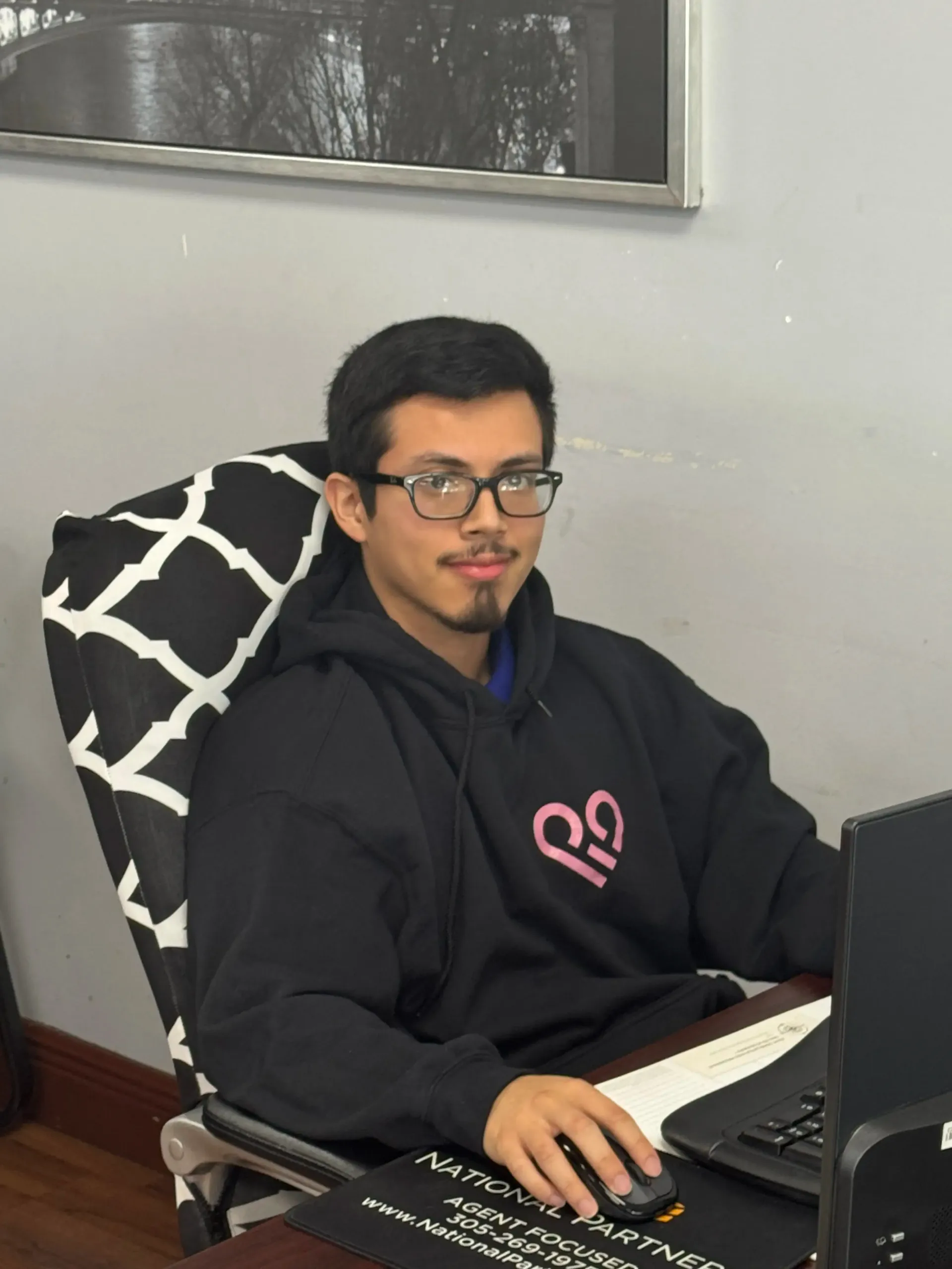 A man wearing glasses is sitting at a desk with a laptop