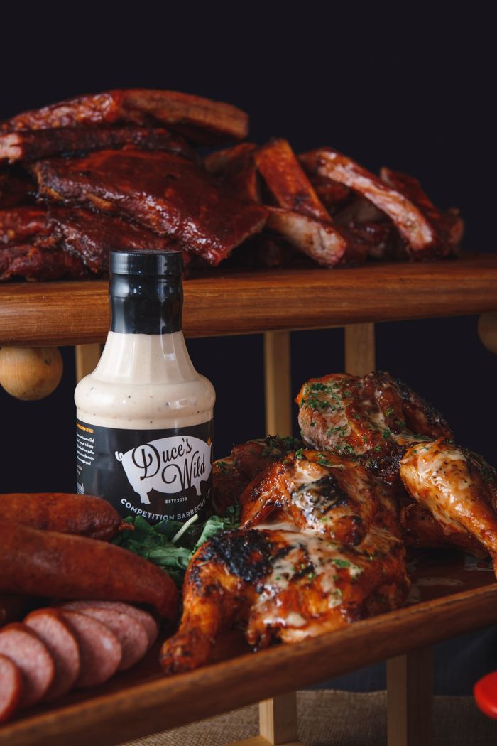 A bottle of ranch dressing is sitting on top of a wooden tray of meat.