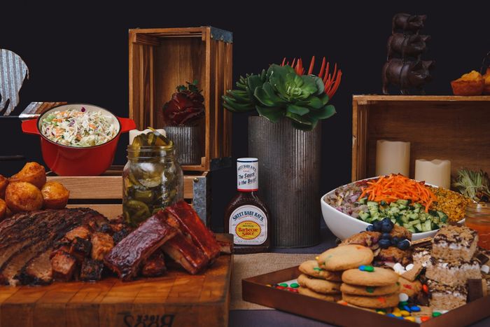 A table topped with a variety of food including meat , vegetables , and cookies.