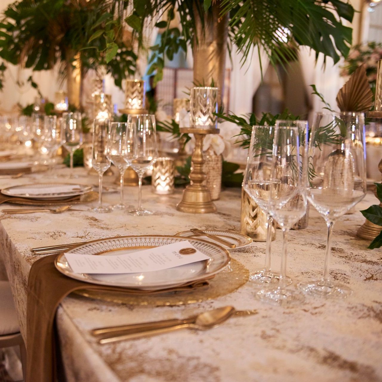A table is set up with gold chargers and flatware with white plates, glassware, and menu cards.