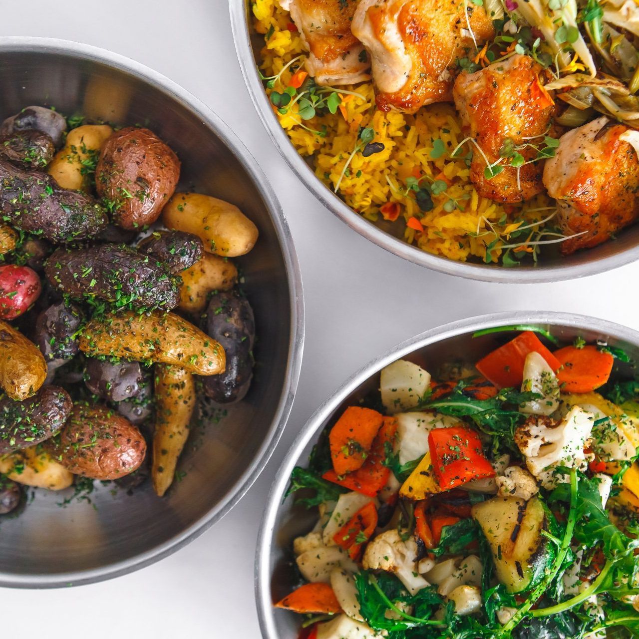 Silver skillets with vegetables, potatoes, and chicken.