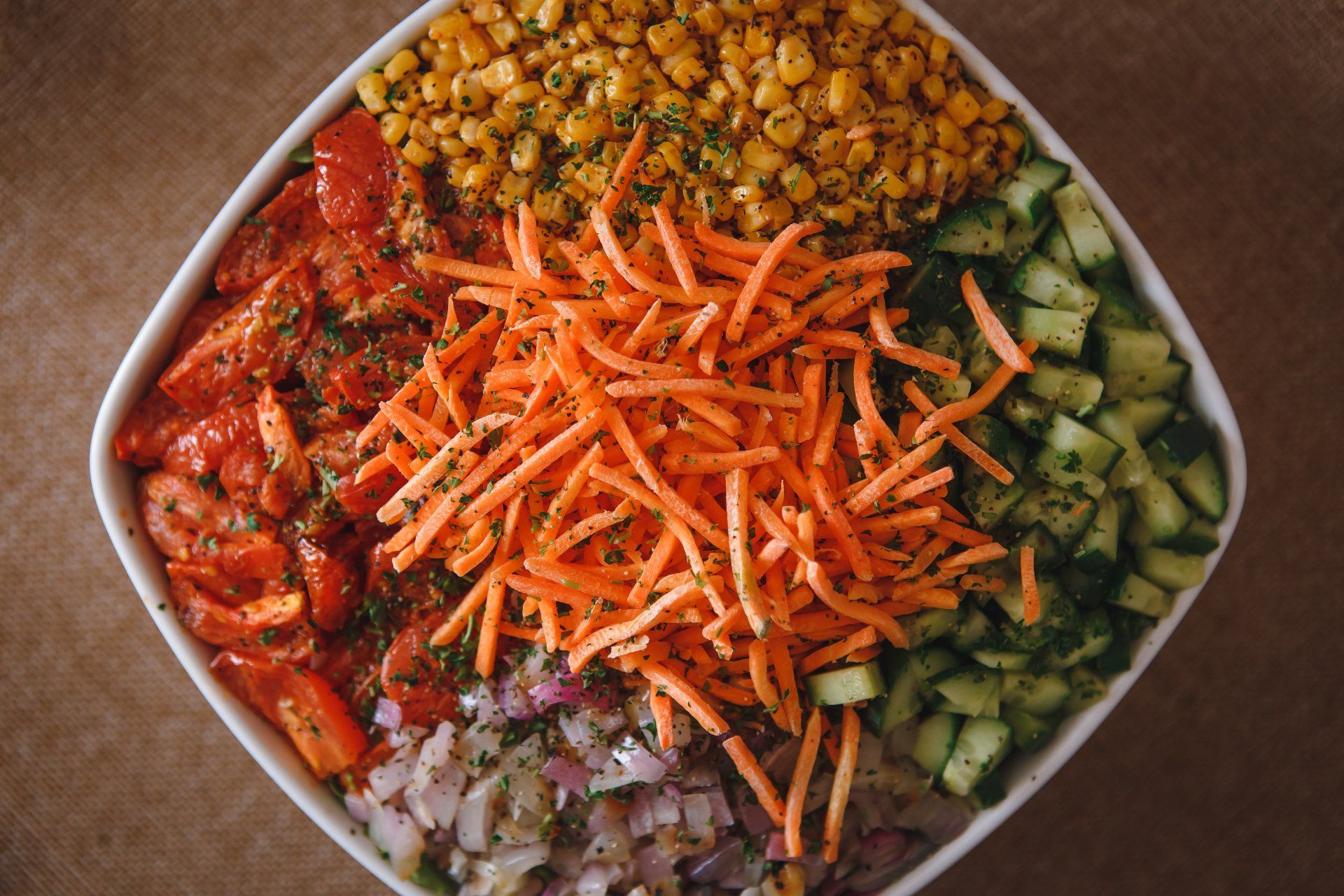 A bowl filled with carrots , corn , onions , cucumbers and tomatoes.