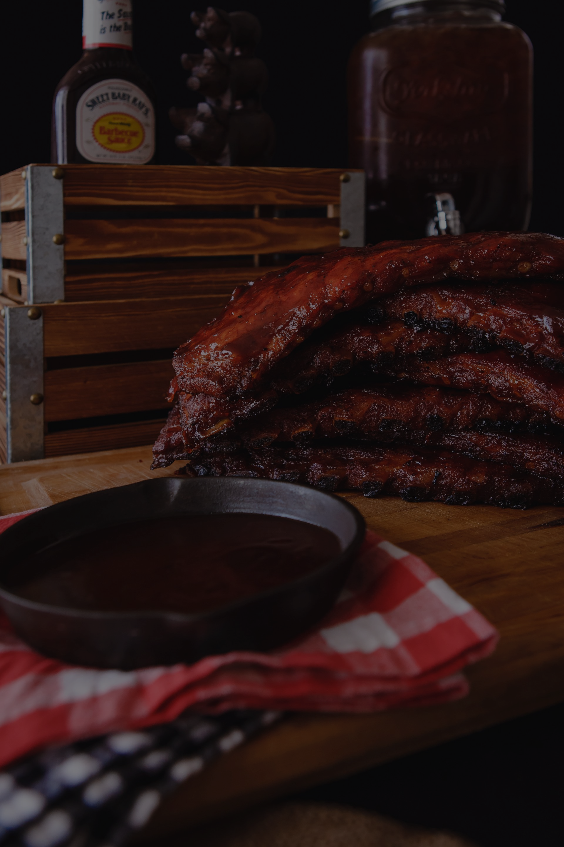A stack of pork ribs sitting on top of a wooden table next to a bowl of barbecue sauce.
