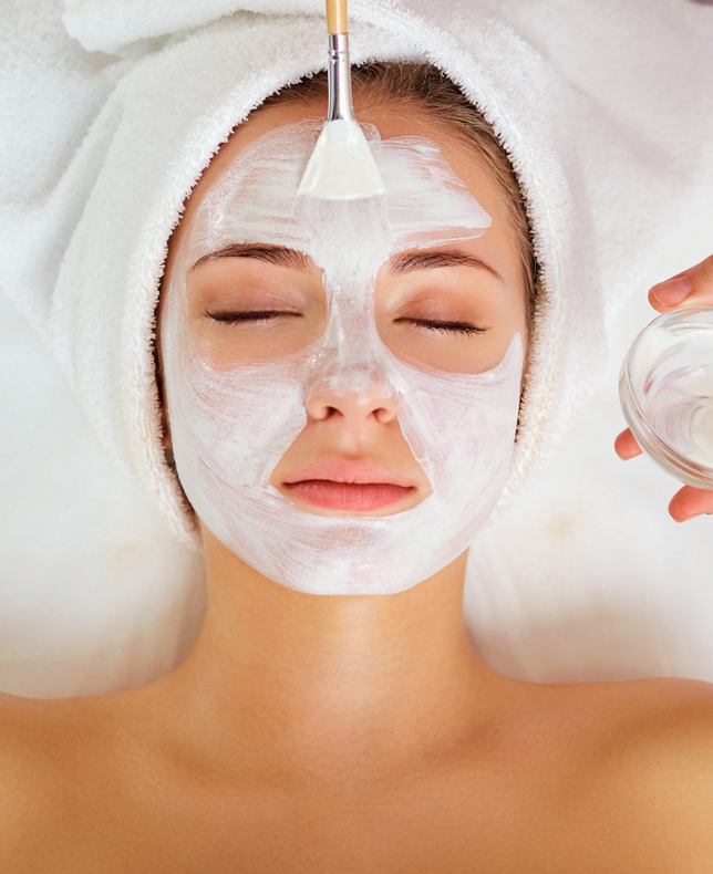 Eine Frau bekommt in einem Spa eine weiße Maske auf das Gesicht aufgetragen.