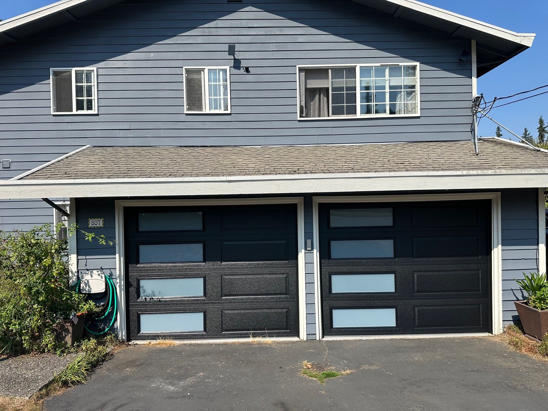 Two-story house with a blue-gray exterior and black garage doors, two windows above.